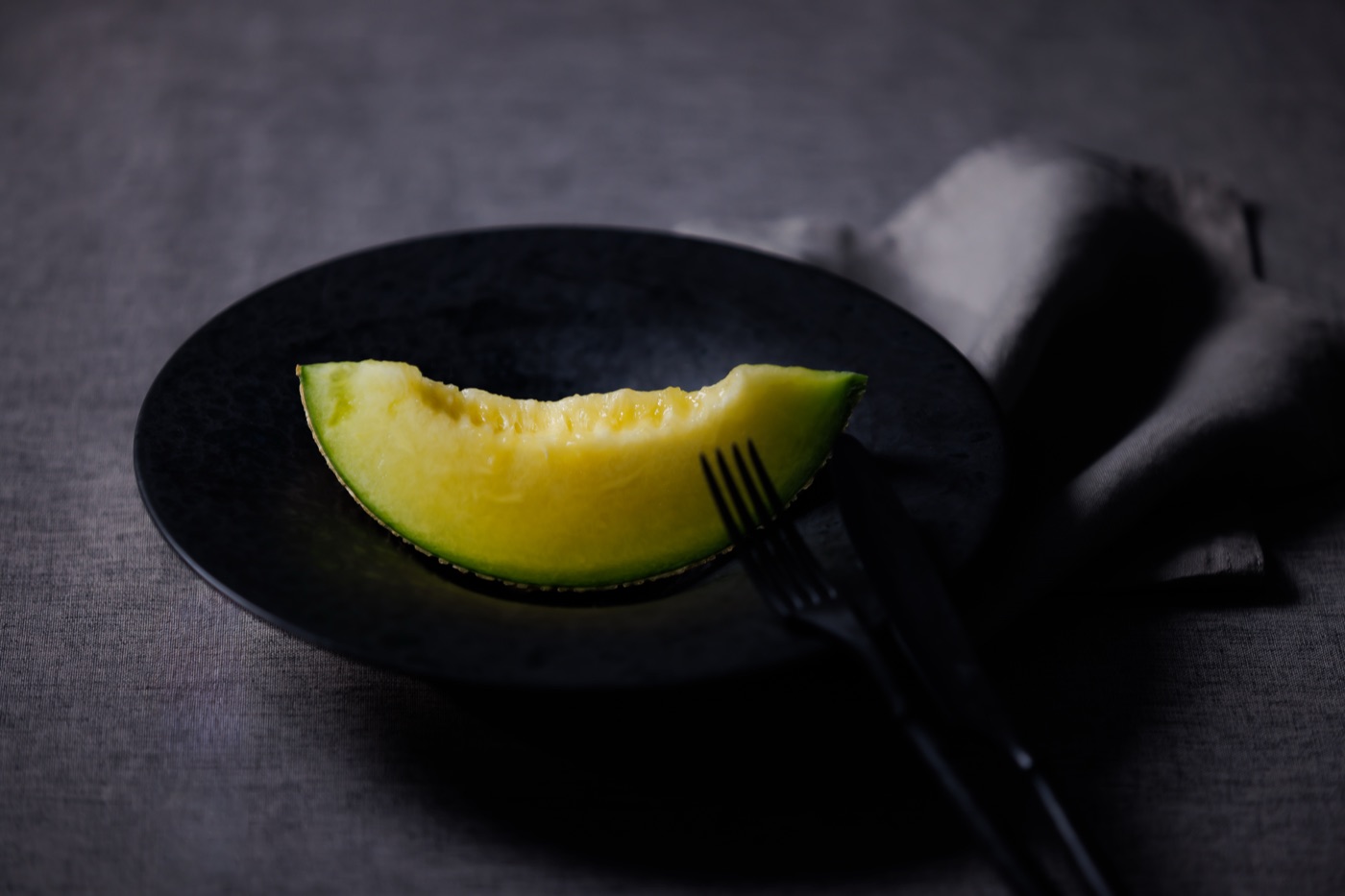 A glistening slice of Crown Melon on a dark ceramic plate